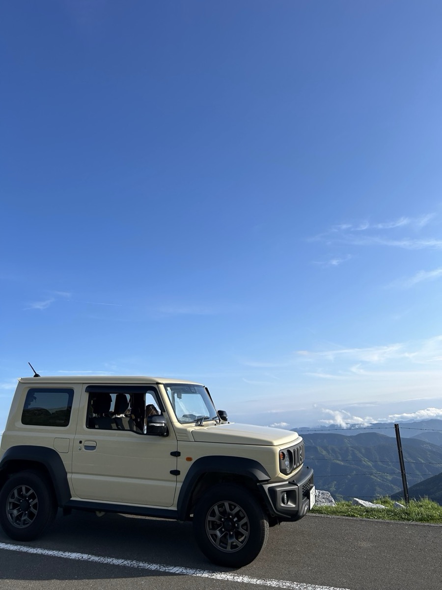 標高の高い山の上に停まるジムニーシエラ。青空と山並みが広がる