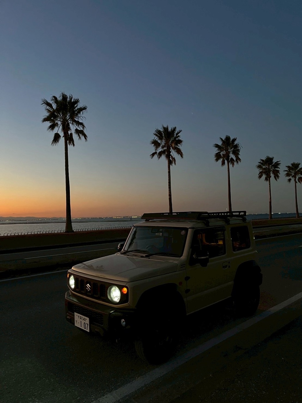 夕暮れのヤシ並木の海沿いを走るジムニーシエラ(JB74)